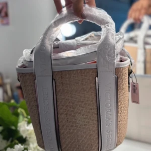Beige och vit väska från Victoria's Secret - Säljer en superfin beige och vit väska från Victoria's Secret. Den har ett snyggt flätat mönster och vita detaljer med texten 'Victoria's Secret' på handtagen. Väskan har en röd insida med blommigt mönster och en justerbar axelrem. Perfekt för sommarens alla äventyr!