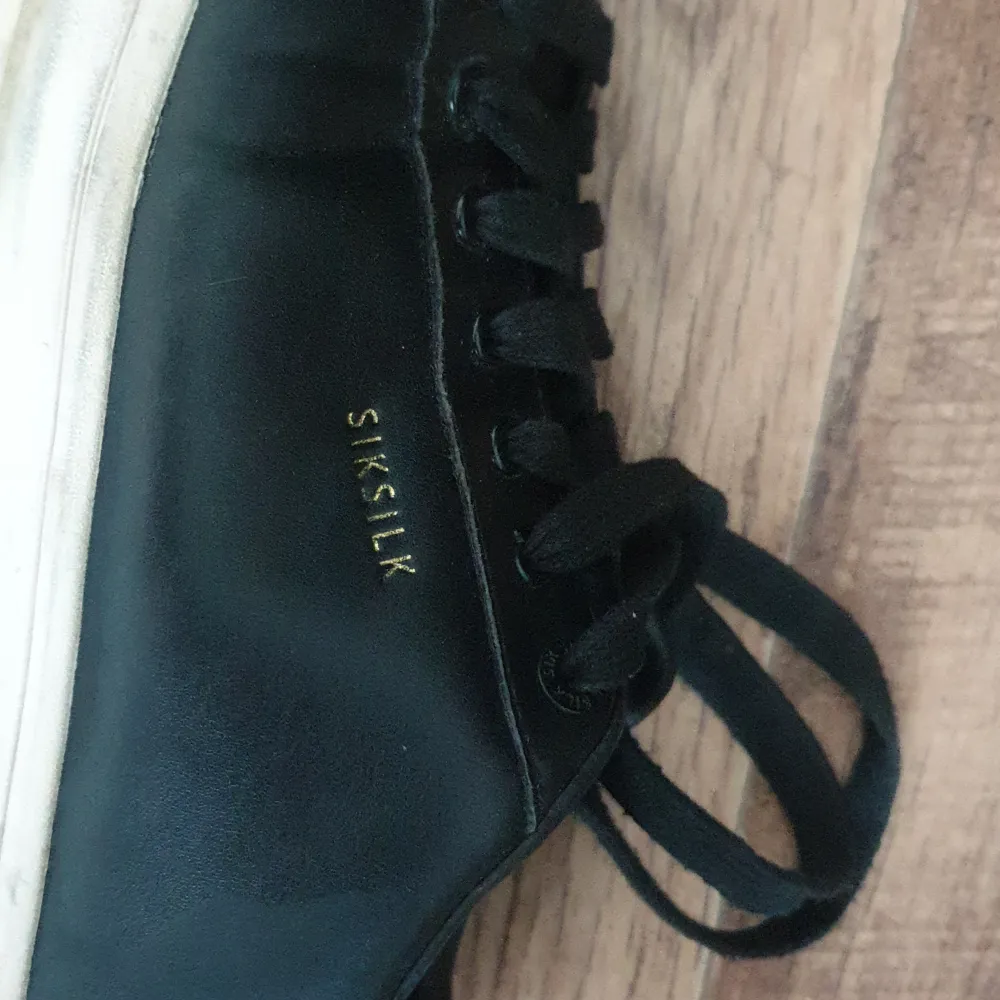 Säljer ett par svarta sneakers från SikSilk. De har en klassisk design med snörning och en vit sula. Skorna är i skinn och har en diskret logga på sidan. Perfekta för vardagsbruk!. Skor.