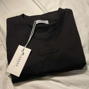 Svart t-shirt från Lanvin - Säljer en snygg svart t-shirt från Lanvin i storlek S. T-shirten är gjord av mjuk bomull och har en broderad Lanvin-logga på bröstet. Perfekt för både vardag och fest! (Helt ny aldrig använd Tagg finns kvar) (pris kan diskuteras) Ny pris 2500 mitt pris 1250 alltså halva butiks priset