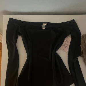 Svart offshoulder festtop från Nelly - Säljer en elegant svart offshoulder top från Nelly. Perfekt för festliga tillfällen med sin stilrena design. Toppen är i nyskick med lappen kvar och har en tight passform som framhäver figuren. Ett måste i garderoben för alla som älskar klassisk stil! 