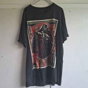 Svart Darth Vader t-shirt från Black Timber - Säljer en svart t-shirt från Black Timber med en stor Darth Vader-tryck på framsidan. T-shirten är i storlek XL och har korta ärmar. Den är lite sliten med ett litet hål på framsidan, men fortfarande cool och perfekt för Star Wars-fans! 🖤