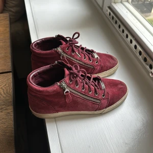 Vinröda Ralph Lauren sneakers  - Säljer ett par snygga vinröda sneakers i mocka med dragkedja på sidorna. Skorna har snörning framtill och en vit sula som ger en cool kontrast. Märket är Ralph Lauren och de är i bra skick men det finns tecken på användning. Perfekta för höst och vår!