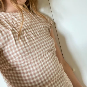 Urban Outfitters klänning - Sötaste rutiga klänningen från Urban Outfitters! Öppen rygg och slits i ena sidan. Är lång men inte hela vägen ner till fötterna. Går in i midjan och kan anpassas baktill med band!🎀💗💃 vit och rosa/ brun