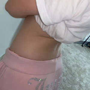 Rosa mjukisbyxor från Juicy Couture - Säljer ett par superbekväma rosa mjukisbyxor från Juicy Couture. De är dekorerade med glittriga stenar som bildar texten 'Juicy' på baksidan. Perfekta för en avslappnad dag hemma eller en chill dag ute. Materialet är mjukt och skönt, och byxorna har en låg midja för en avslappnad passform.