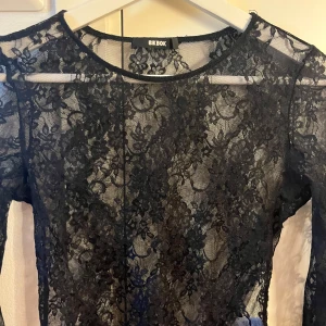 Svart spetsbody från Bik Bok - Säljer en elegant svart spetsbody från Bik Bok. Den är långärmad och har ett vackert blommigt mönster. Perfekt för en festlig kväll eller en utekväll med vänner. Bodyn är i storlek S och sitter tight för en smickrande passform.