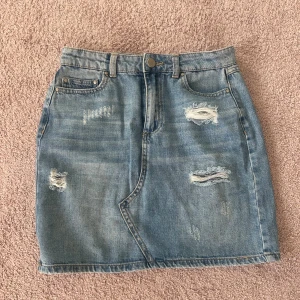 Jeanskjol - En fin jeanskjol från Vila med slitningar som fina detaljer. Jeansfärgad och i ett bra skick, då den endast är använd en gång. Den perfekta jeanskjolen!