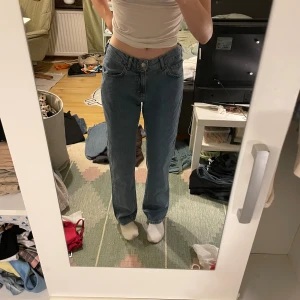 Blå jeans med låg midja - Säljer ett par snygga blå jeans från Bikbok med låg midja och rak passform. De är i storlek 28/32 och har en klassisk design med knappar och dragkedja. Perfekta för en avslappnad stil!