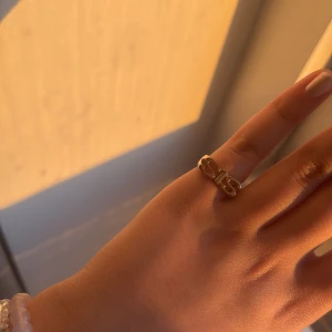 Guldfärgad ring med rosett - Elegant guldfärgad ring med en stilren rosettdetalj. Perfekt för att ge en touch av glamour till din outfit. Passar utmärkt för både vardag och speciella tillfällen.