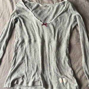 Odd Molly tröja - Säljer en grå ribbad tröja med en söt röd rosett vid halsringningen. Tröjan har långa ärmar och ett tryck med texten 'Lost on Purpose'. Perfekt för en avslappnad stil. Passar S/M har inga defekter