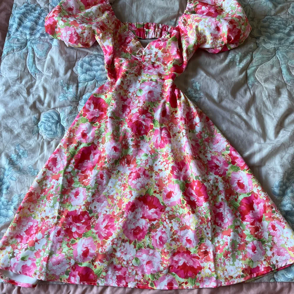 Charmig blommig klänning i rosa och gröna toner med puffiga kortärmar och en öppen rygg. Klänningen har en v-ringad design och är perfekt för sommarens festligheter. I nytt skick💕. Mekot.