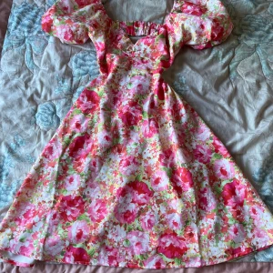 Blommig klänning med puffärmar - Charmig blommig klänning i rosa och gröna toner med puffiga kortärmar och en öppen rygg. Klänningen har en v-ringad design och är perfekt för sommarens festligheter. I nytt skick💕