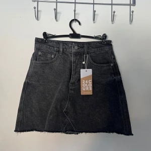 Svart jeanskjol från 24 Colours - Snygg svart jeanskjol från 24 Colours med rå kant och klassisk femficksdesign. Kjolen har en knappgylf. Passar bra till olika stilar och tillfällen. Storlek XS,S i nytt skick 