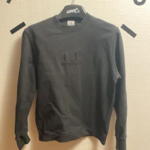 Svart tröja från C.P. Company - Säljer en stilren svart tröja från C.P. Company. Tröjan har en klassisk design med rund hals och långa ärmar. Passar xs-s. Inga defekter men lite ut torkad/solblekt. Pris kan diskuteras 