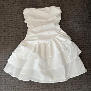 Vit klänning - Vit axelbandslös klänning med volanger. Perfekt för sommaren och superfint som studentklänning! Aldrig använd! Nypris 230 kr