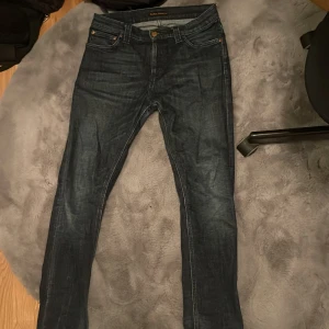 Mörkblå jeans från Nudie Jeans - Snygga mörkblå jeans från Nudie Jeans med klassisk femficksdesign. De har en knappgylf och är tillverkade i slitstarkt denim. Perfekta för en stilren look.