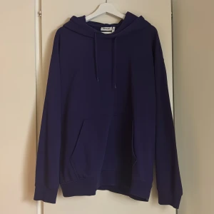 Lila hoodie från Weekday - Säljer en stilren lila hoodie från Weekday. Den har en klassisk design med en stor ficka framtill och justerbar huva. Perfekt för en avslappnad look.