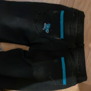 Svarta lågmidjade jeans med blå detaljer - Snygga svarta lågmidjade jeans med unika blå detaljer på bakfickorna. Perfekta för en cool och avslappnad stil. De har en klassisk femficksdesign och en bekväm passform.