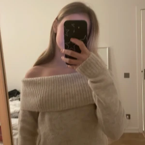 Beige offshoulder stickad tröja - Säljer en mysig beige stickad tröja med offshoulder-design. Tröjan har långa ärmar och en bred ribbad kant vid halsen och nederkanten. Perfekt för kyliga dagar!
