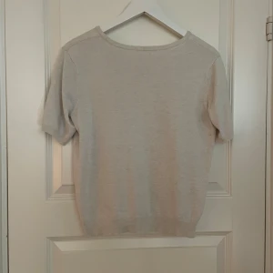 Beige kortärmad tröja - Säljer en stilren beige tröja med korta ärmar. Perfekt för en avslappnad look. Tröjan har en rund hals och ribbade kanter vid ärmslut och nederkant.