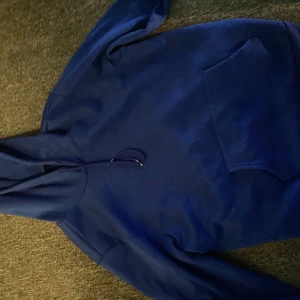 Blå hoodie - Säljer en klassisk blå hoodie med känguruficka framtill. Perfekt för en avslappnad stil och bekväm att bära. Den har en justerbar huva med dragsko.