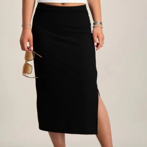 Svart ribbad kjol - Snygg svart ribbad kjol med slits på sidan. Perfekt för en stilren look. Kjolen har en tight passform och är knälång, vilket ger en elegant siluett.