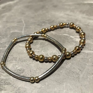 Tvåfärgat armband i guld och silver - Snyggt armband i både guld och silver. Ena armbandet har en stilren design med släta silverstavar och små gulddetaljer, medan det andra består av guldfärgade pärlor. Perfekt för att ge en elegant touch till din outfit. 100kr för båda 50kr för ett
