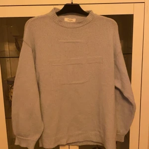 Ljusblå stickad tröja från Lis Bonne - Vacker stickad Ljusblå tröja från Lis Bonne Atelier med en stor bokstav ”B” framtill. Tröjan har en rund halsringning och långa ärmar med muddar. Använt skick. Storlek xs oversized Nypris 1500kr