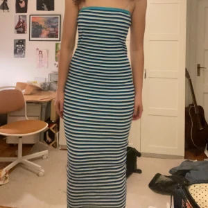 Randig axelbandslös maxiklänning - Snygg axelbandslös klänning med blå och vita ränder. Perfekt för en somrig look. Klänningen är lång och har en tight passform. 
