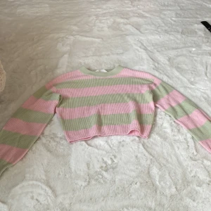 Randig croppad tröja från H&M - Säljer en söt randig tröja från H&M i rosa och grönt. Tröjan är croppad och har långa ärmar med ribbade muddar. Perfekt för en avslappnad stil.