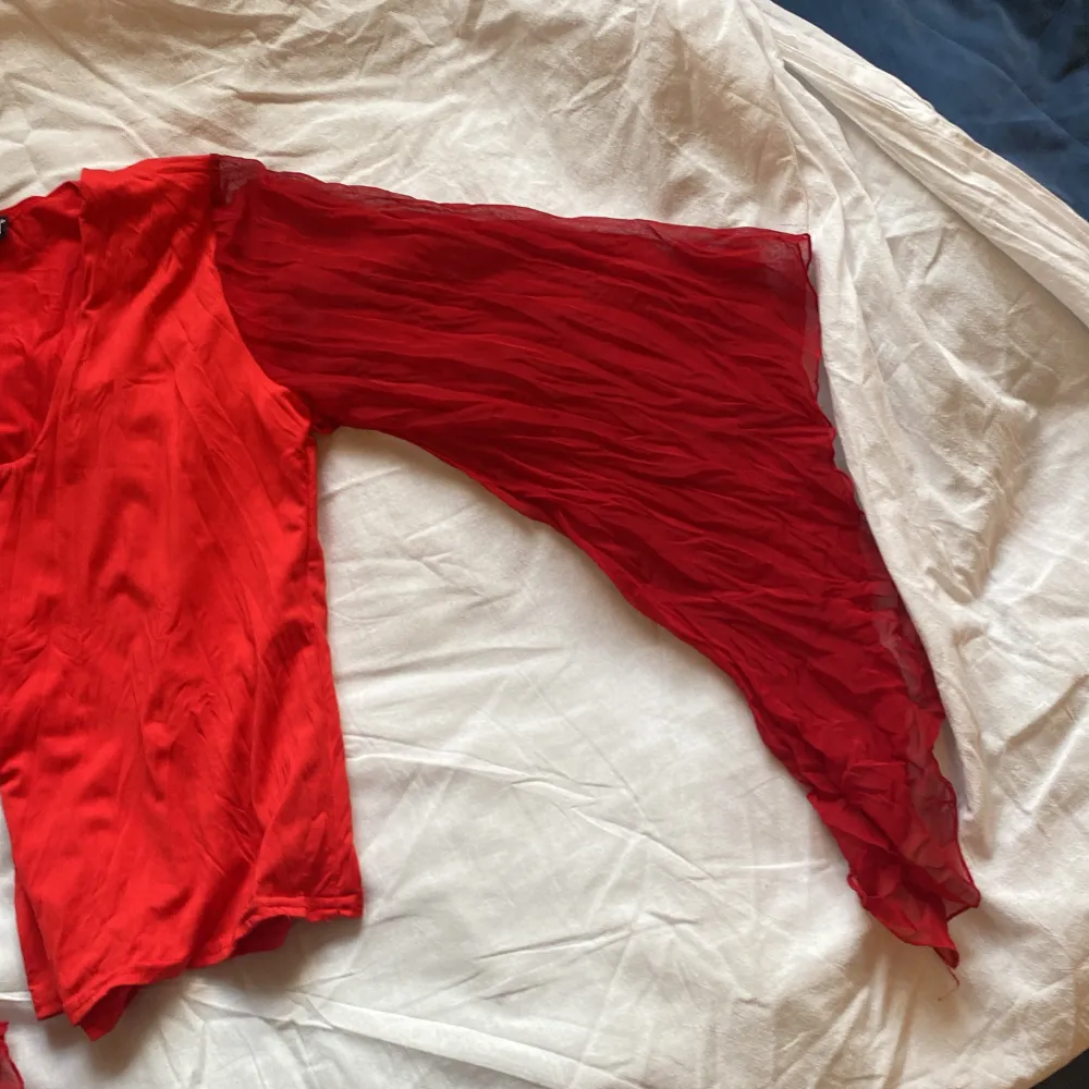 Säljer en snygg röd blus med vida, transparenta ärmar och v-ringning. Perfekt för att sticka ut med sin unika design och livfulla färg.. Yläosat.
