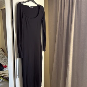 Svart långärmad klänning från NA-KD - Snygg svart långärmad klänning från NA-KD i en tight passform. Klänningen har en rund halsringning och är perfekt för en stilren look. Tillverkad i ett ribbat material som ger en skön känsla. Perfekt för både vardag och fest! Klänningen går under knäna men över anklarna. 