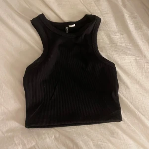 Svart ribbad linnetopp från Divided - Snygg svart ribbad linnetopp från Divided. Perfekt för en stilren look med sin ärmlösa design och croppade längd. Passar utmärkt till både jeans och kjol.