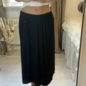 Svart långkjol från Gina Tricot - Snygg svart långkjol från Gina Tricot i storlek XS. Kjolen har en elastisk midja och ett elegant, plisserat tyg som ger ett stilrent fall. Perfekt för att skapa en chic look.