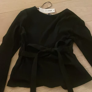 Svart långärmad topp från Gina Tricot - Snygg svart långärmad topp från Gina Tricot med knytband i midjan. Aldrig använd och har prislapp kvar. Säljer för halva priset 