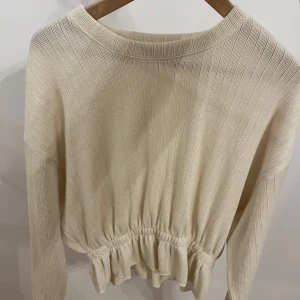 Beige ribbad tröja - Säljer en stilren beige ribbad tröja med långa ärmar och elastisk midja. Perfekt för en avslappnad look. Passar 32-36