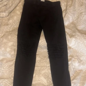 Svarta leggings från Lindex Kids - Säljer ett par svarta leggings från Lindex Kids. De har en snygg rynkad detalj på knäna som ger en unik look. Perfekta för vardagsbruk och bekväma att bära.