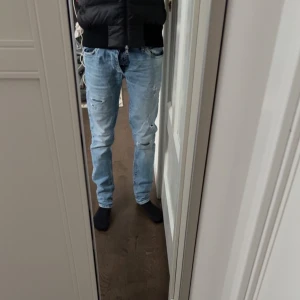 Ljusblå jeans med slitningar från Jack & Jones  - Säljer ett par ljusblå jeans med coola slitningar och en klassisk femficksdesign. De har en dragkedja och knapp framtill. Perfekta för en avslappnad stil. Dem är riktigt feta och i otroligt skick. Hör av er vid frågor 
