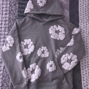 Grå hoodie med vita molnmönster - Säljer en grå hoodie med unika vita molnmönster. Tröjan har en klassisk huva och en stor ficka framtill. Perfekt för en avslappnad stil och mysiga dagar. Passar bra till jeans eller mjukisbyxor.