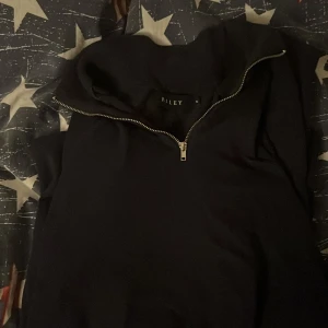 En marinblå halfzip från Riley - Säljer en stilren svart tröja från Riley med dragkedja. Perfekt för en avslappnad look. Tröjan har en hög krage och långa ärmar.