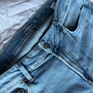 Blå jeans från Dressmann - Snygga ljusblå jeans från Dressmann med klassisk femficksdesign. De har en knappgylf och är perfekta för en avslappnad stil. Passar bra till både t-shirt och skjorta. Slimfit