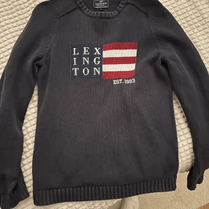 Lexington tröja  - Säljer en snygg mörkblå tröja från Lexington med ett broderat märke på framsidan. Tröjan har långa ärmar och ribbade kanter vid hals, ärmslut och nederkant. Perfekt för en stilren look!