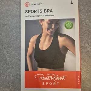 Svart sport-bh från Pierre Robert strl L - Säljer en svart sport-bh från Pierre Robert med mid-high support och sömlös design. Perfekt för träning med Max Dry-teknologi för att hålla dig torr och bekväm. Tillverkad av återvunnet material. Nypris 399kr