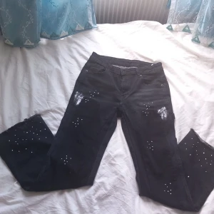 Flare denim - Coola svarta jeans med unika slitningar och vita stänkdetaljer. Byxorna har en straight passform och är perfekta för en streetwear stil. De har klassisk femficksdesign och knappgylf. Pris kan diskuteras