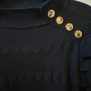 Svart stickad topp från Yu & Me - Snygg svart stickad tröja från Yu & Me med dekorativa guldknappar på axeln. Tröjan har ett unikt mönster och volangdetaljer på ärmarna som ger en trendig look. Står storlek S/M men skulle säga att den mer passar XS/S. Aldrig använd 💕