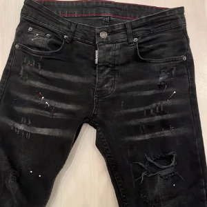 Svarta jeans från dsquared2  - Snygga svarta jeans från Dsquared2 med coola slitningar och detaljer. De har också röda detaljer på sig.