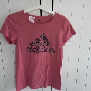Rosa t-shirt från Adidas - Säljer en rosa t-shirt från Adidas med ett leopardmönstrat logotryck på framsidan. T-shirten är tillverkad i bomull