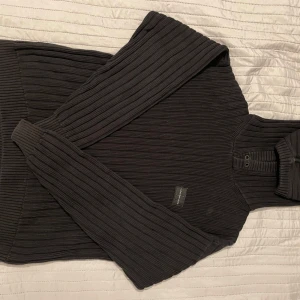 Svart ribbad hoodie från Calvin Klein Jeans - Säljer en stilren svart ribbad hoodie från Calvin Klein Jeans. Tröjan har långa ärmar och en klassisk design med knappar vid halsen. Perfekt för en avslappnad men ändå snygg look.