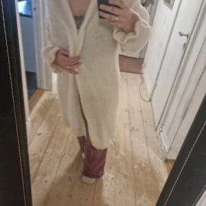 Vit stickad kofta - Mysig vit stickad kofta med långa ärmar och en avslappnad passform. Perfekt för kyliga dagar när du vill hålla dig varm och bekväm. Koftan har en enkel design som gör den lätt att matcha med olika outfits.