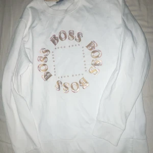 Hugo boss kofta - Säljer min vita sweatshirt från Hugo Boss med ett coolt BOSS-tryck i cirkel på framsidan. Tröjan har långa ärmar och en klassisk rund halsringning. Perfekt för en avslappnad stil.Ny pris 1499