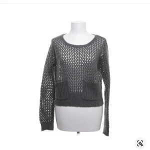 Grå stickad tröja från Monki - Säljer en grå stickad tröja från Monki med ett öppet stickmönster och två fickor framtill. Tröjan har långa ärmar och en rund halsringning. Perfekt för lager-på-lager-stil!